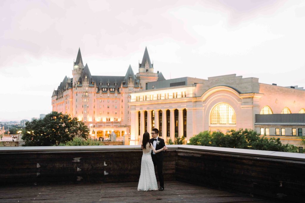 Bride and groom dancing on an open-air rooftop with illuminated Château Laurier.