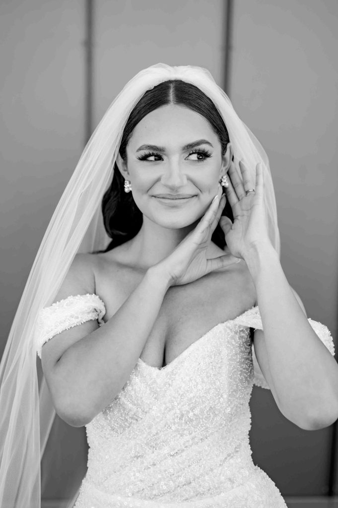 A black-and-white close-up of the bride adjusting her veil with a soft smile.