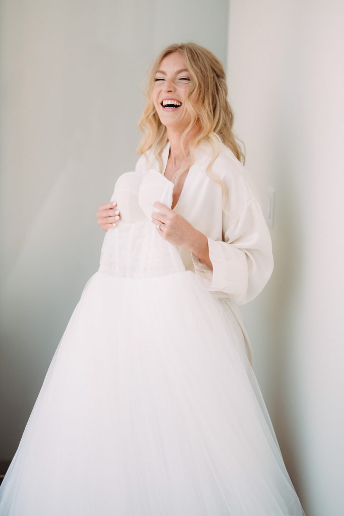 The bride laughs joyfully while holding her wedding gown, her happiness shining through.